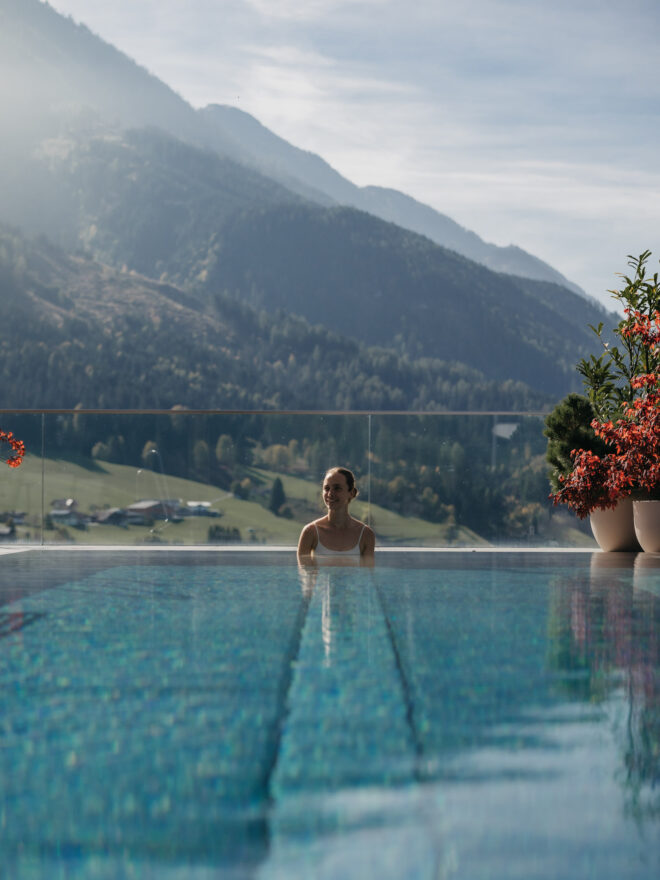 Frau sitzt im Rooftop Pool mit Bergpanorama im Hintergrund